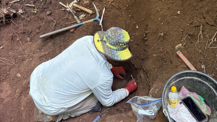 Overhead view of a miner in a bucket hat kneeling in a dirt pit digging by hand